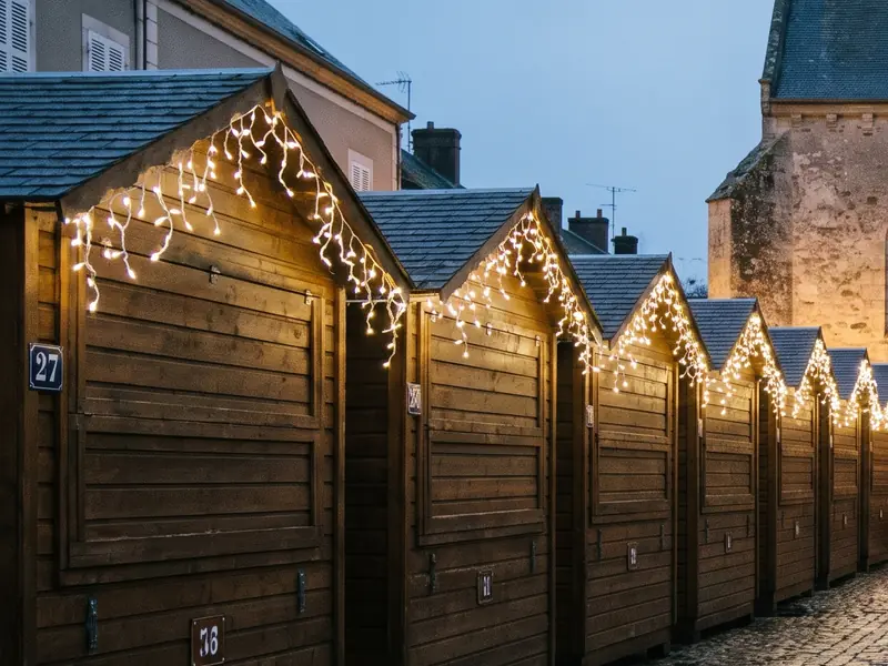 Une place de village au crépuscule, avec une rangée de chalets de marché de Noël numérotés.