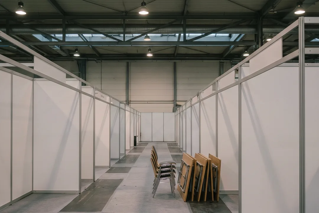 An empty exhibition hall before opening, booths built, chairs and tables still stacked in the aisle.